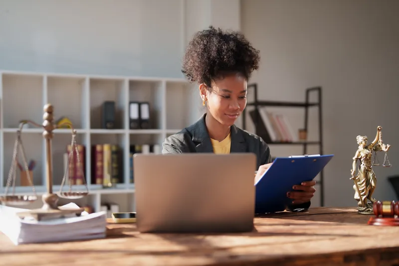 A lawyer at her desk working through a binder of records beside a laptop