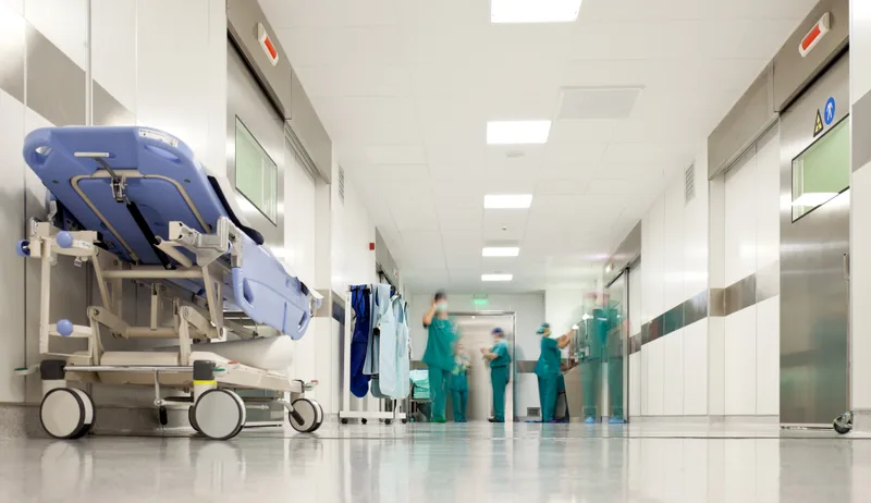 A long, bright hospital corridor with staff in scrubs at the far end