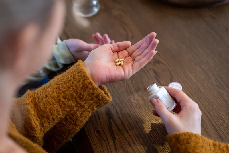 A person holding capsules in one palm and a prescription bottle in the other hand
