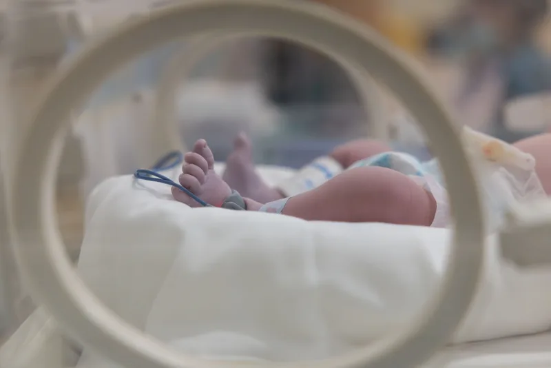 A newborn's feet seen through the round port of a neonatal incubator