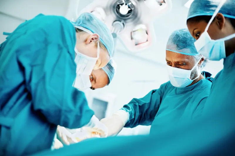 A surgical team in masks and caps working under operating room lights