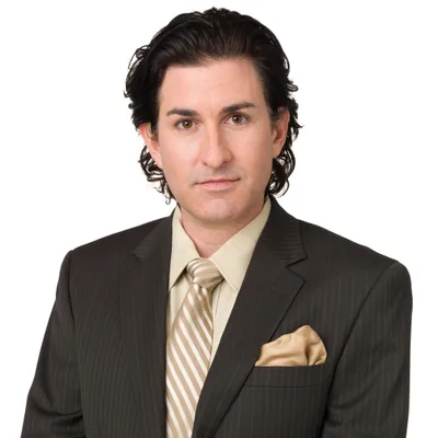 Marcus J. Delgado, a trial attorney with dark shoulder-length hair, wearing a brown suit with a gold striped tie and pocket square