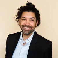 Daniel Osei, a smiling man with curly hair and a salt-and-pepper beard, wearing a navy blazer over an open-collared shirt