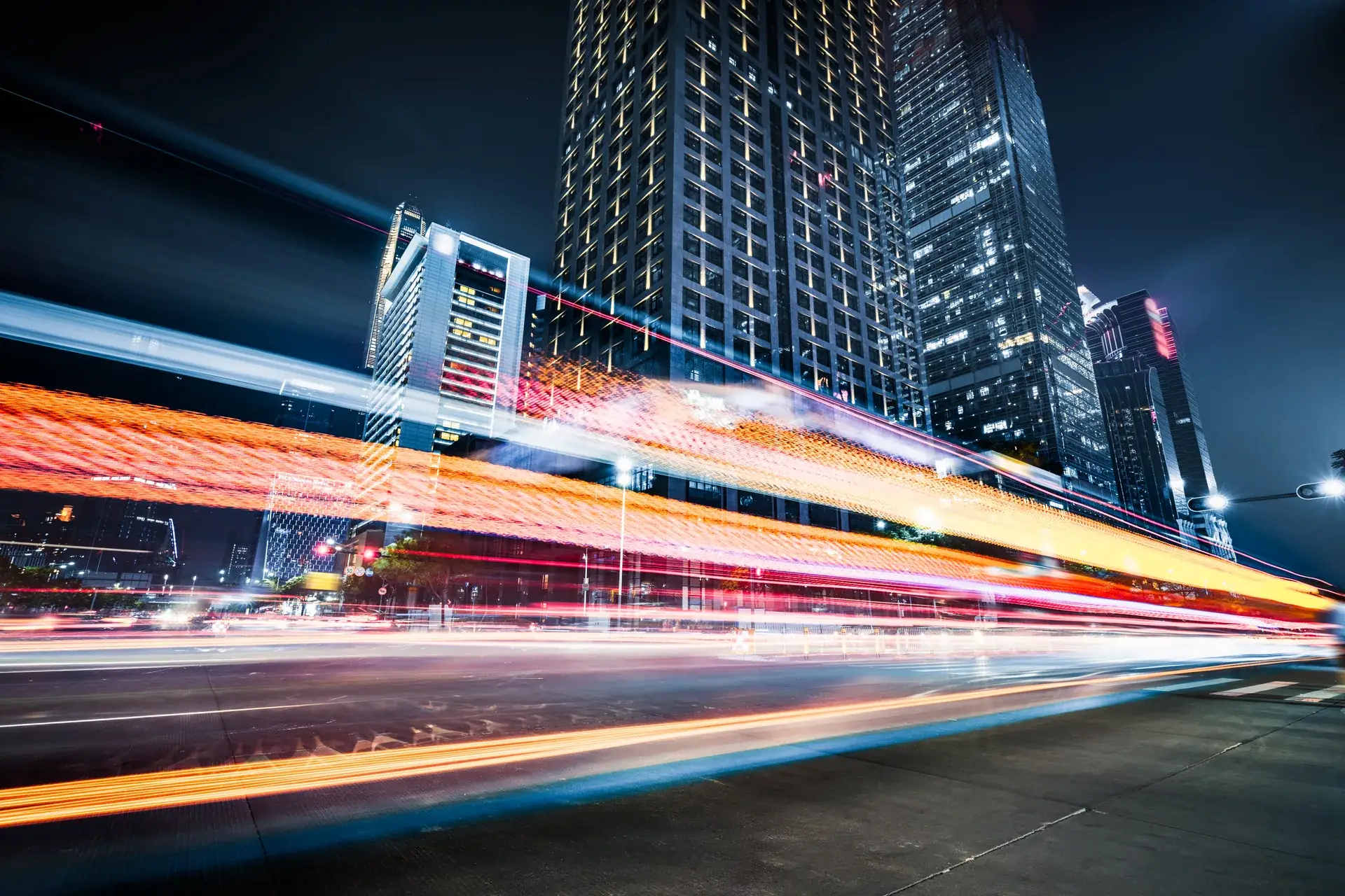 Light trails of fast-moving night traffic streaking beneath office towers on a New York avenue