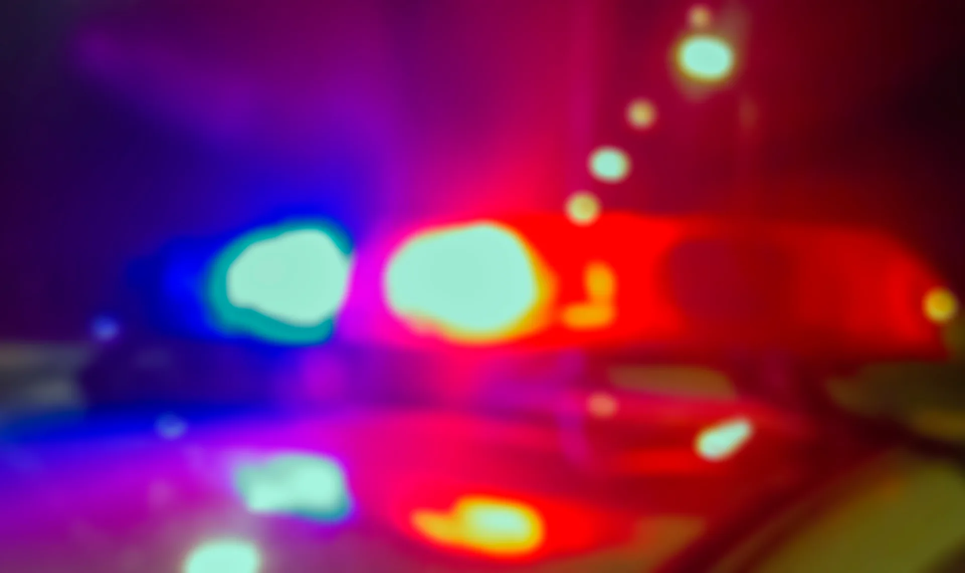 Red and blue emergency lights of a police cruiser glowing against the dark at a night-time accident scene