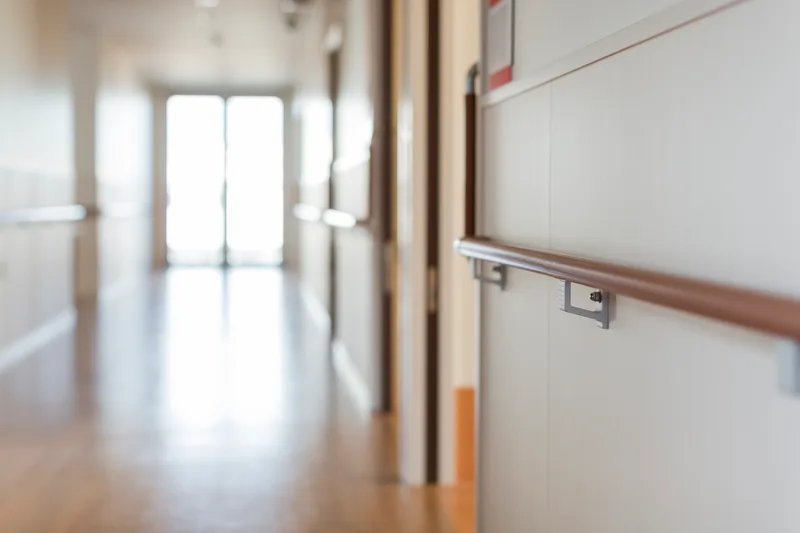 A bright, quiet hallway with a wooden handrail inside a care residence