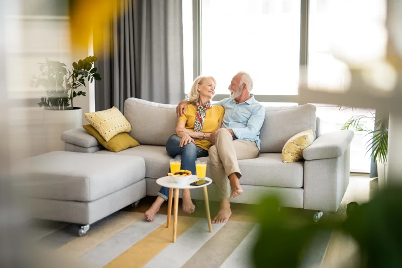 An older couple sitting close together and talking on the sofa in their sunny living room