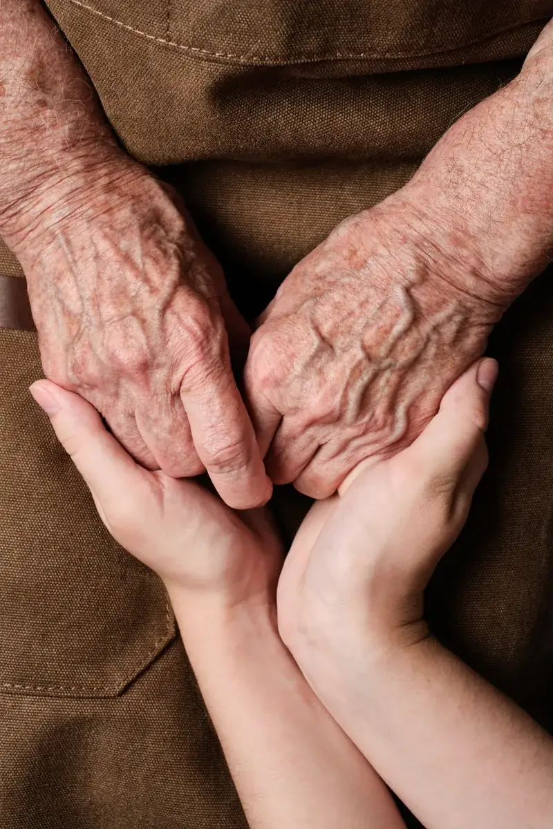 Close view of a younger person's hands gently holding the hands of an older adult