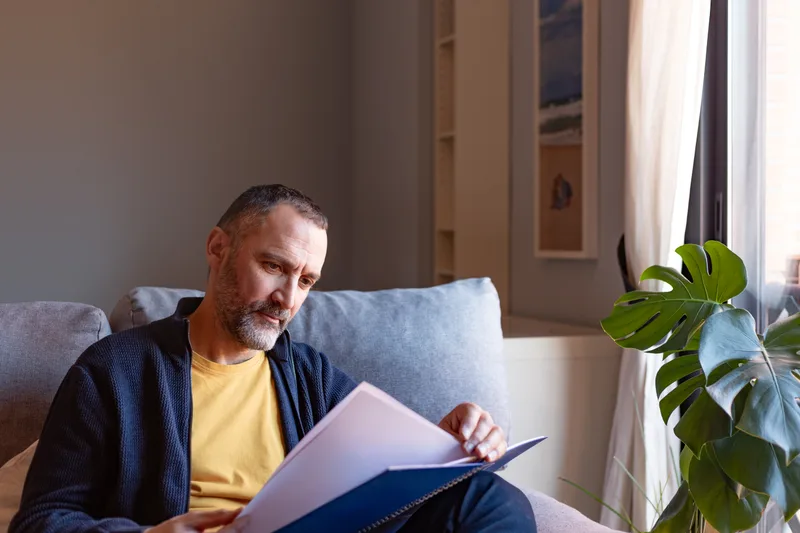 A man sitting on a sofa reads through a folder of papers at home