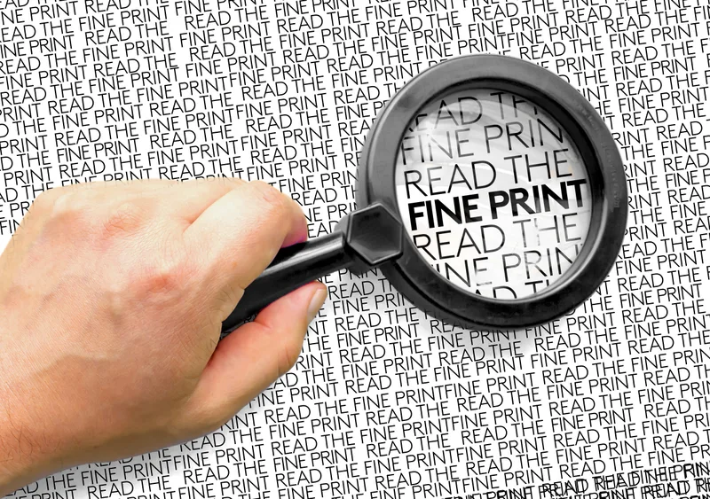 A hand holding a magnifying glass over a page that repeats the words read the fine print