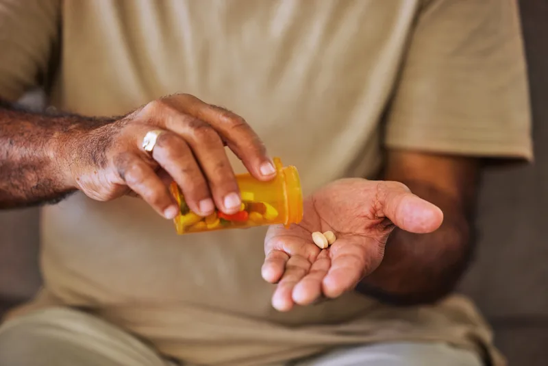 A person tipping two tablets from an orange prescription bottle into their palm