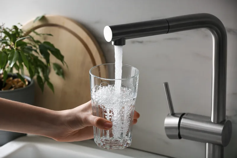 A hand filling a drinking glass from a kitchen tap