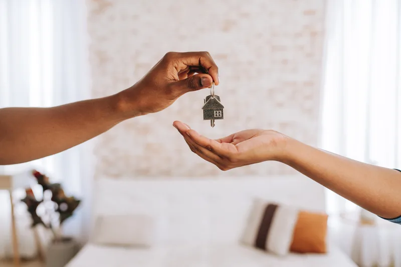 One hand passing a house key on a small key ring into another open hand