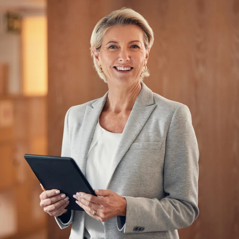 Portrait of Helen Marsh, a smiling woman with blonde hair in a light grey blazer holding a tablet