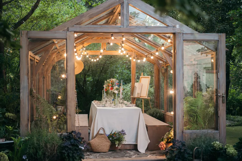 Glass-and-timber conservatory at dusk with string lights over a dinner table dressed in white linen