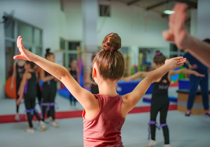 Kids in a movement class stretching their arms wide while an instructor demonstrates at the front of the studio