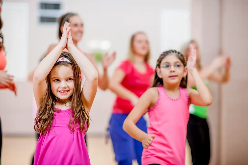 Two smiling kids clapping and dancing in a bright studio during the Saturday kids' movement hour