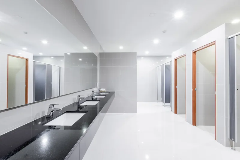 Clean commercial restroom with a long row of sinks, a wide mirror and stall doors