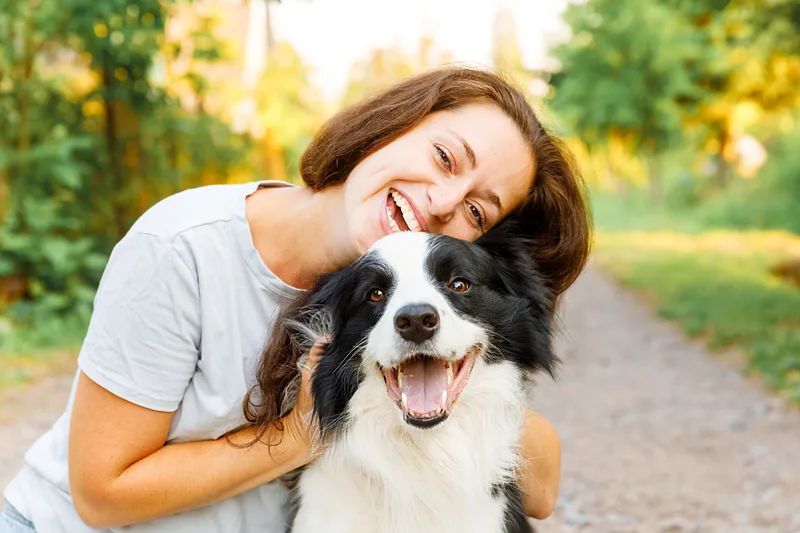 Smiling woman hugging her happy border collie on a sunny park path