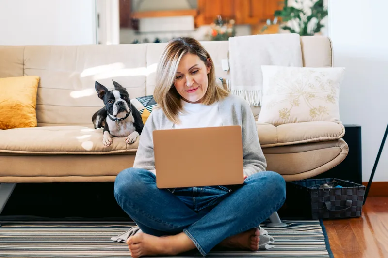 Owner sitting on her living room floor on a video training call while her Boston terrier watches from the sofa