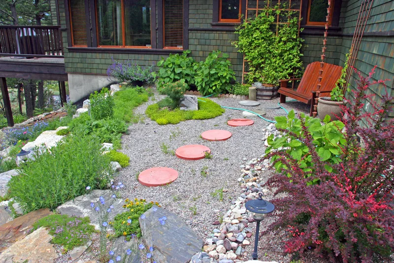 A finished front garden with gravel, stepping stones, low perennials and a red-leaved shrub beside a house