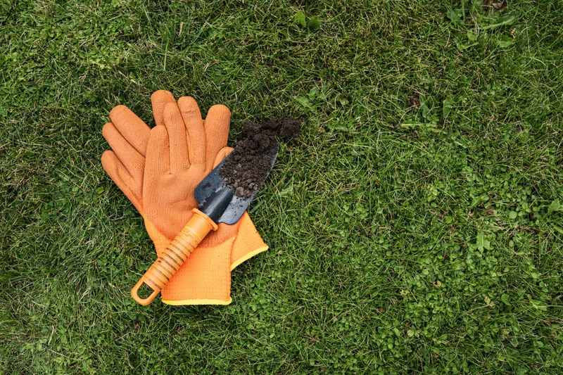 Orange gardening gloves and a hand trowel with fresh soil lying on green grass