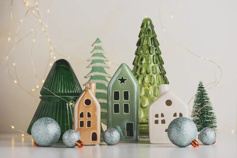 Small ceramic houses and ceramic trees with silver ornaments, part of a holiday display