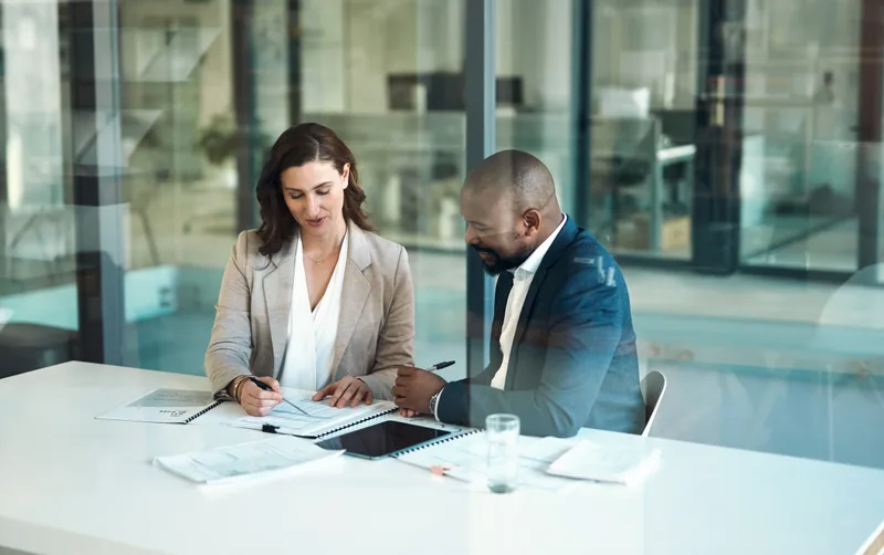 Two professionals reviewing documents together in a glass-walled office
