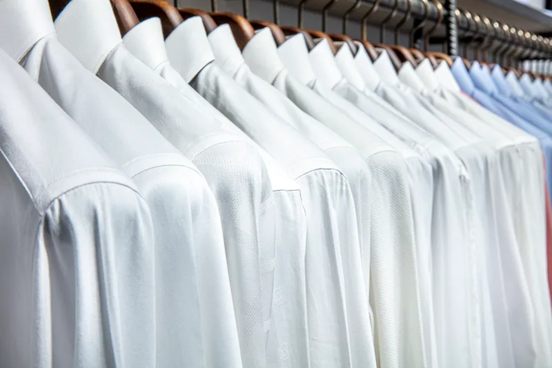 Rail of freshly pressed white and blue dress shirts on wooden hangers at Quickline Dry Cleaners