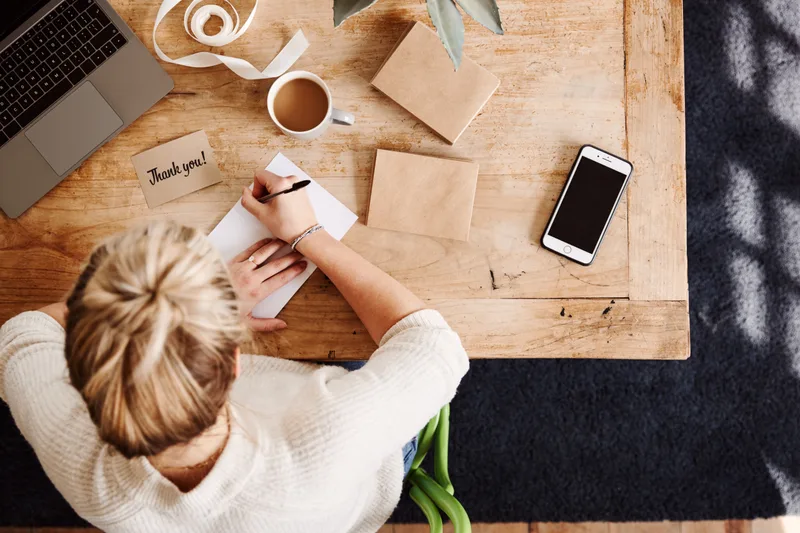Overhead view of a florist hand-writing a small thank-you card at a wooden table
