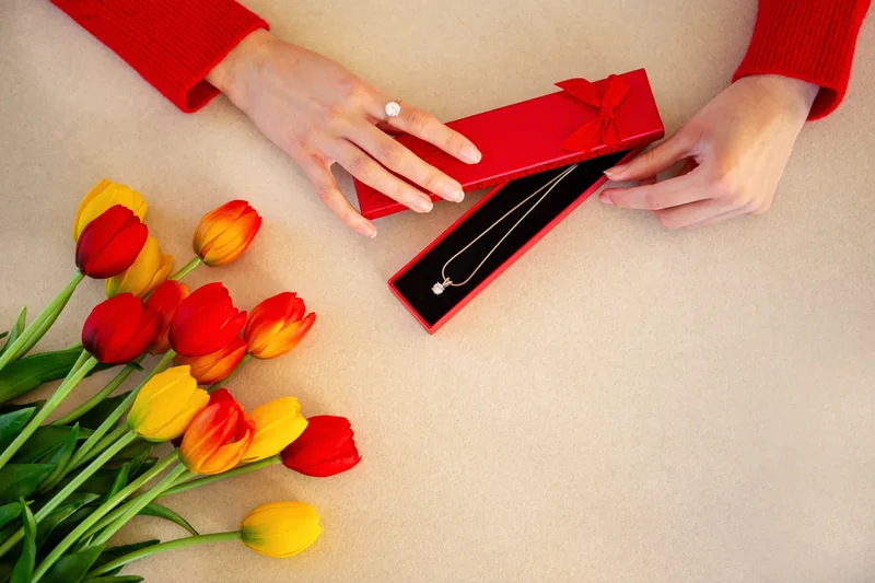 Red and yellow tulips beside a red gift box on a beige table