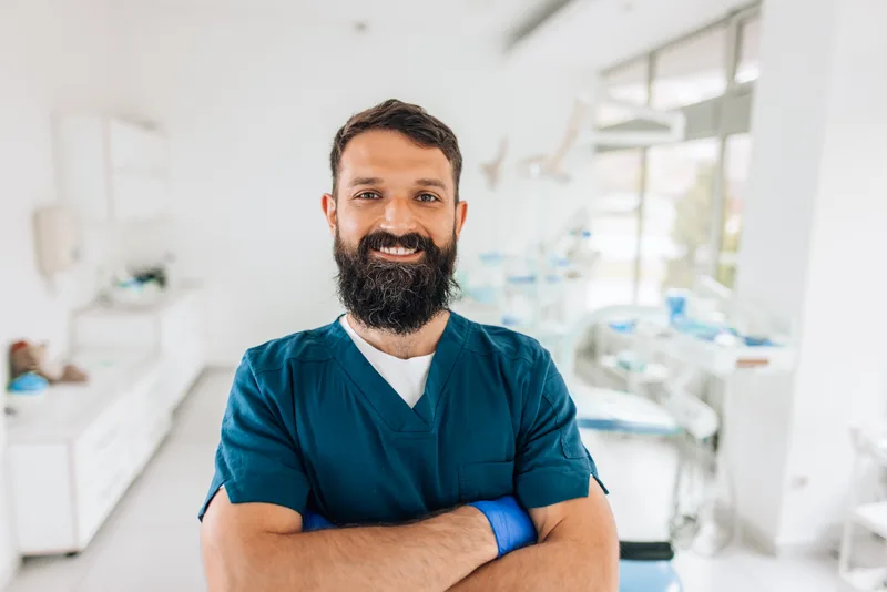Dr. Daniel Brant, a bearded dentist in teal scrubs, smiling in his treatment room