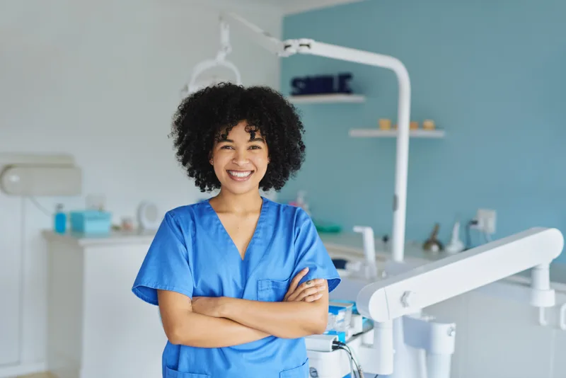 Dr. Amara Osei in blue scrubs, arms crossed and smiling in a treatment room