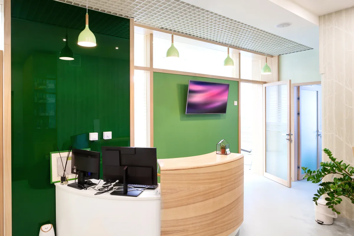 The Polished Dental Co reception — a curved light-wood desk against a deep green wall with mint pendant lights