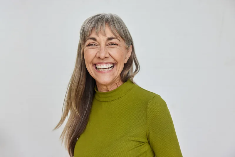 A silver-haired patient laughing freely, showing off bright, healthy teeth