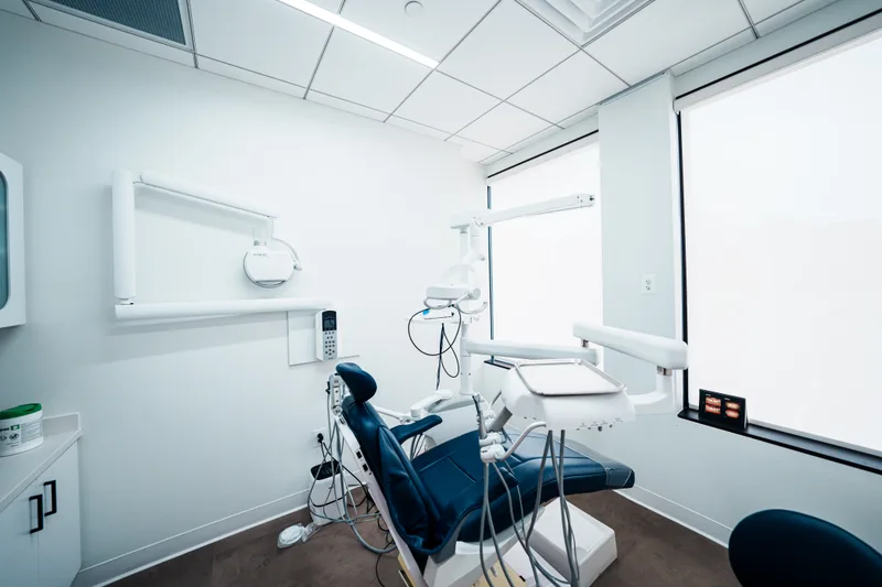 A bright treatment room with a navy dental chair beside a wall of frosted windows