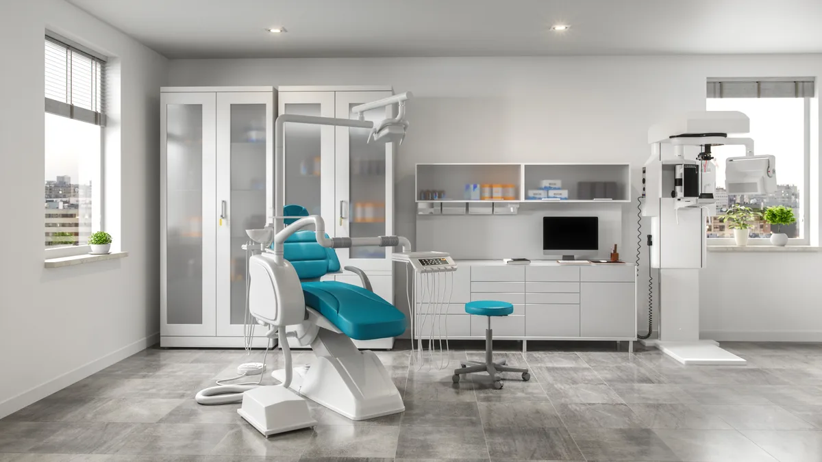 A modern treatment room with a teal dental chair, digital imaging station, and city windows