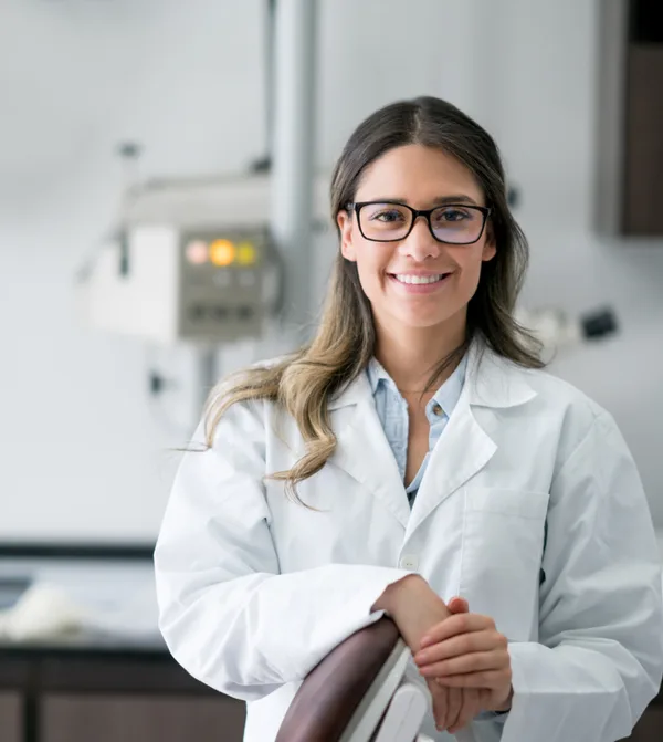 Dr. Elena Ruiz in a white coat and glasses, smiling in front of the imaging suite
