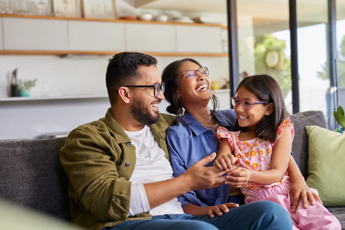 A mom, dad, and daughter laughing together on their living-room couch