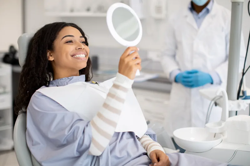A patient smiling at her reflection in a hand mirror after cosmetic treatment