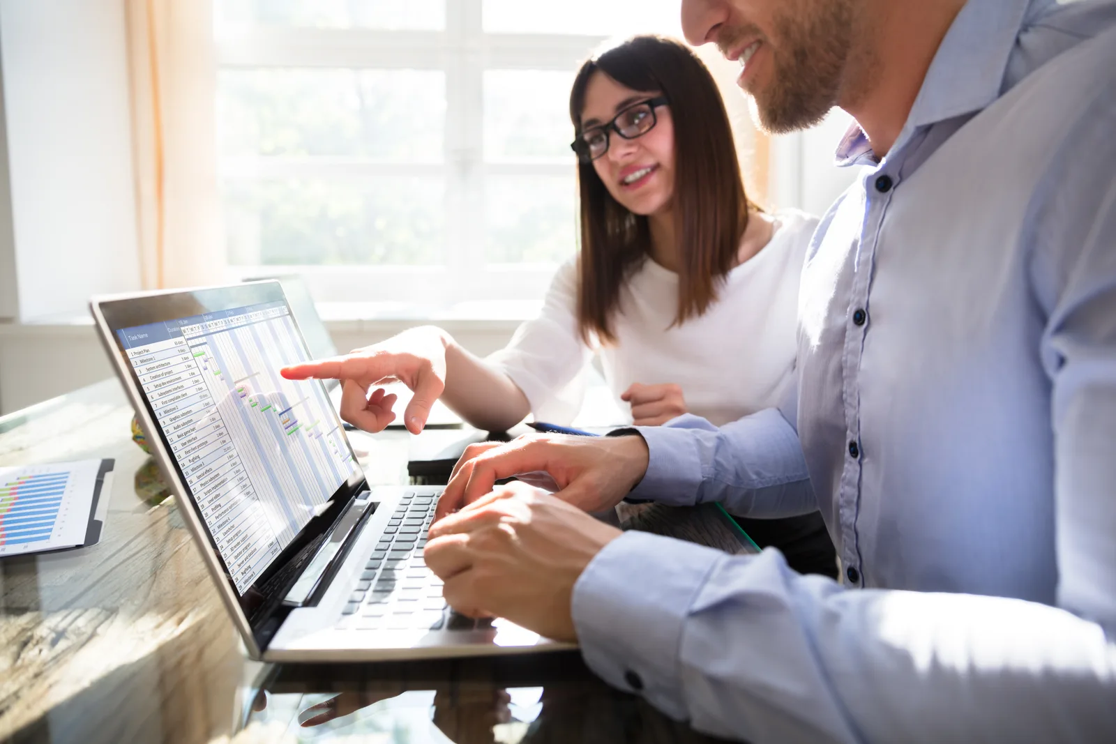 Software team reviewing a client task and deadline workflow dashboard together at a laptop in their office