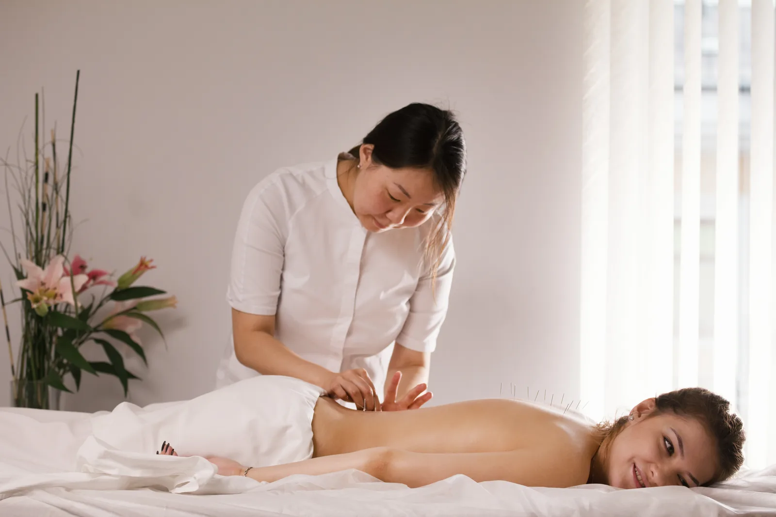 Acupuncturist inserting fine needles into a patient's back during a treatment session in a calm clinic room