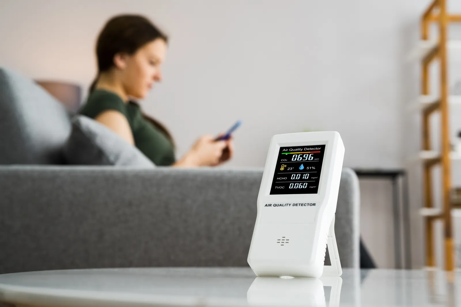 Technician holding a handheld air quality meter to check particulate and VOC readings in a home's living room