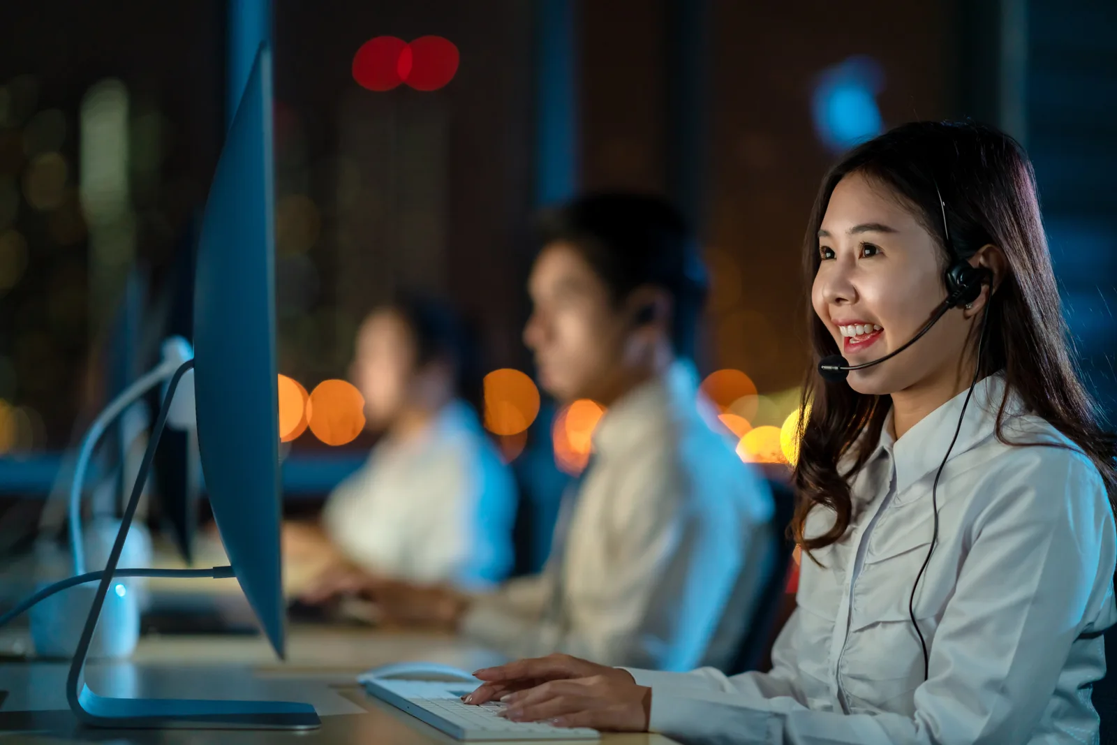 Virtual receptionist wearing a headset and answering a call at a computer workstation in a bright office