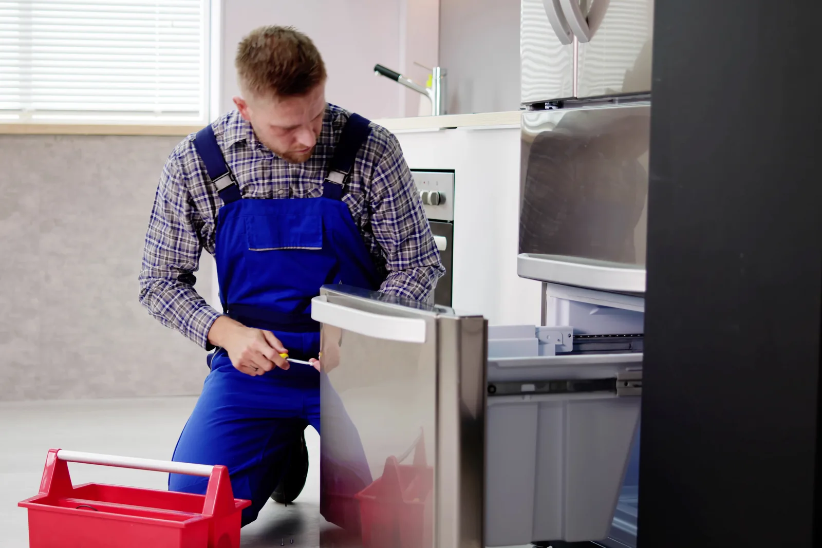 Appliance repair technician testing a repaired refrigerator with a multimeter in a customer's kitchen