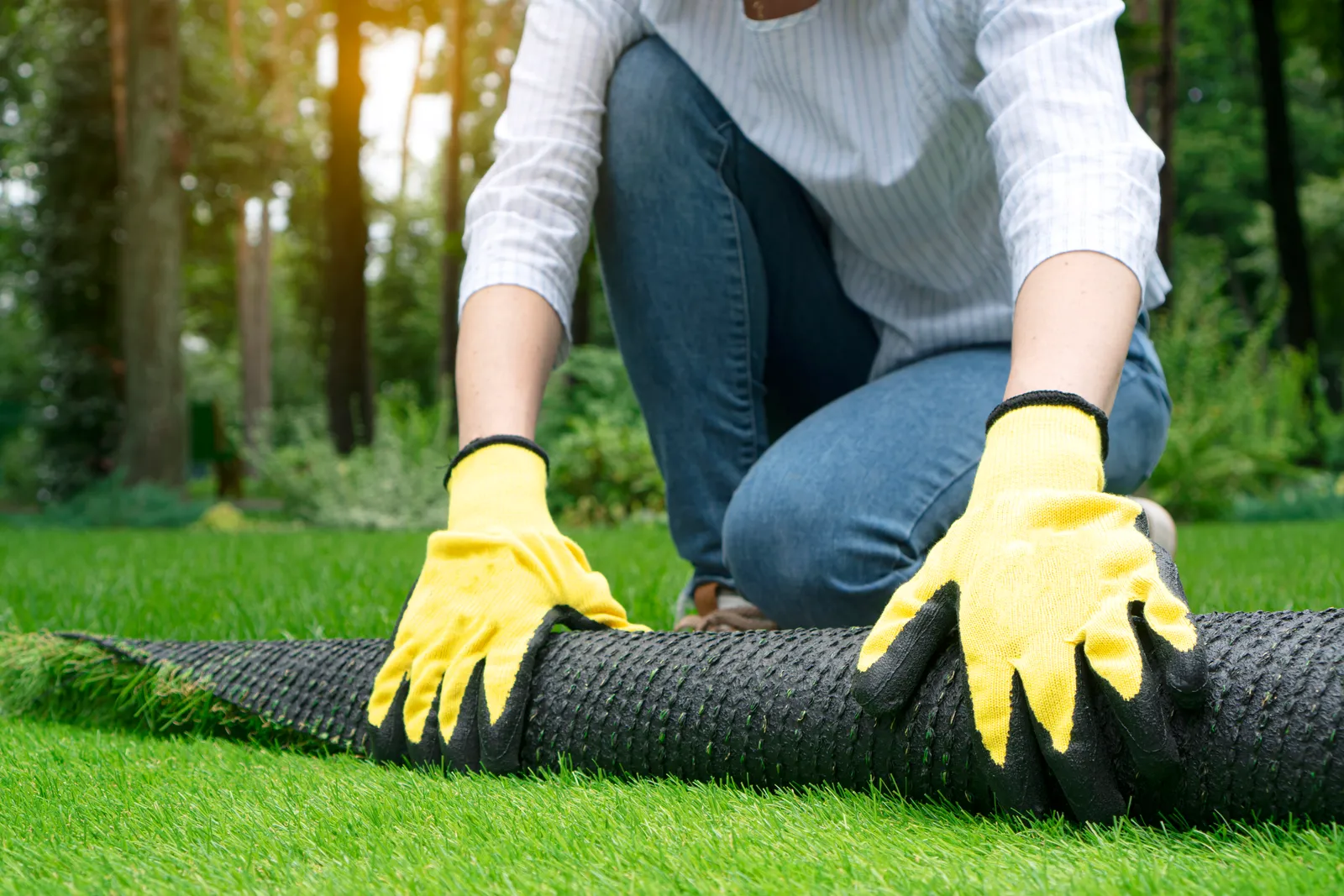 Installer rolling out a strip of artificial turf and brushing the seam flat in a residential backyard