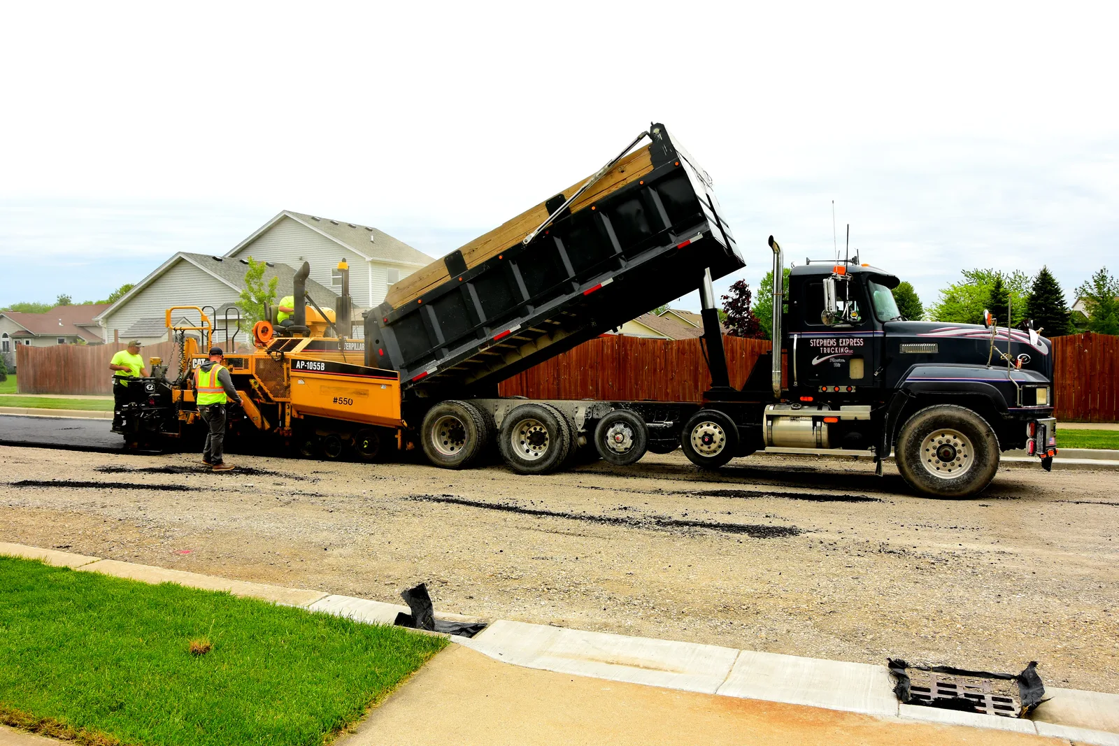 Paving crew laying hot asphalt with a paver machine while a roller compacts the fresh blacktop behind them