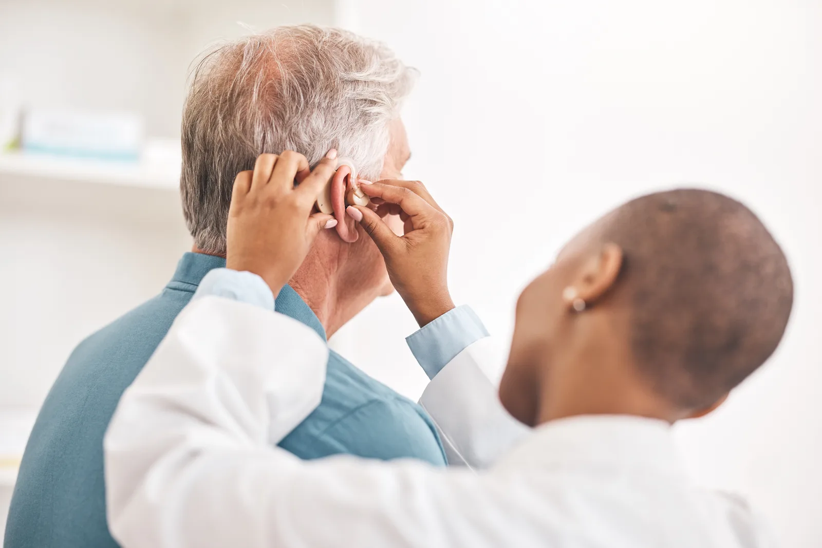 Audiologist fitting a hearing aid behind a seated patient's ear during an appointment