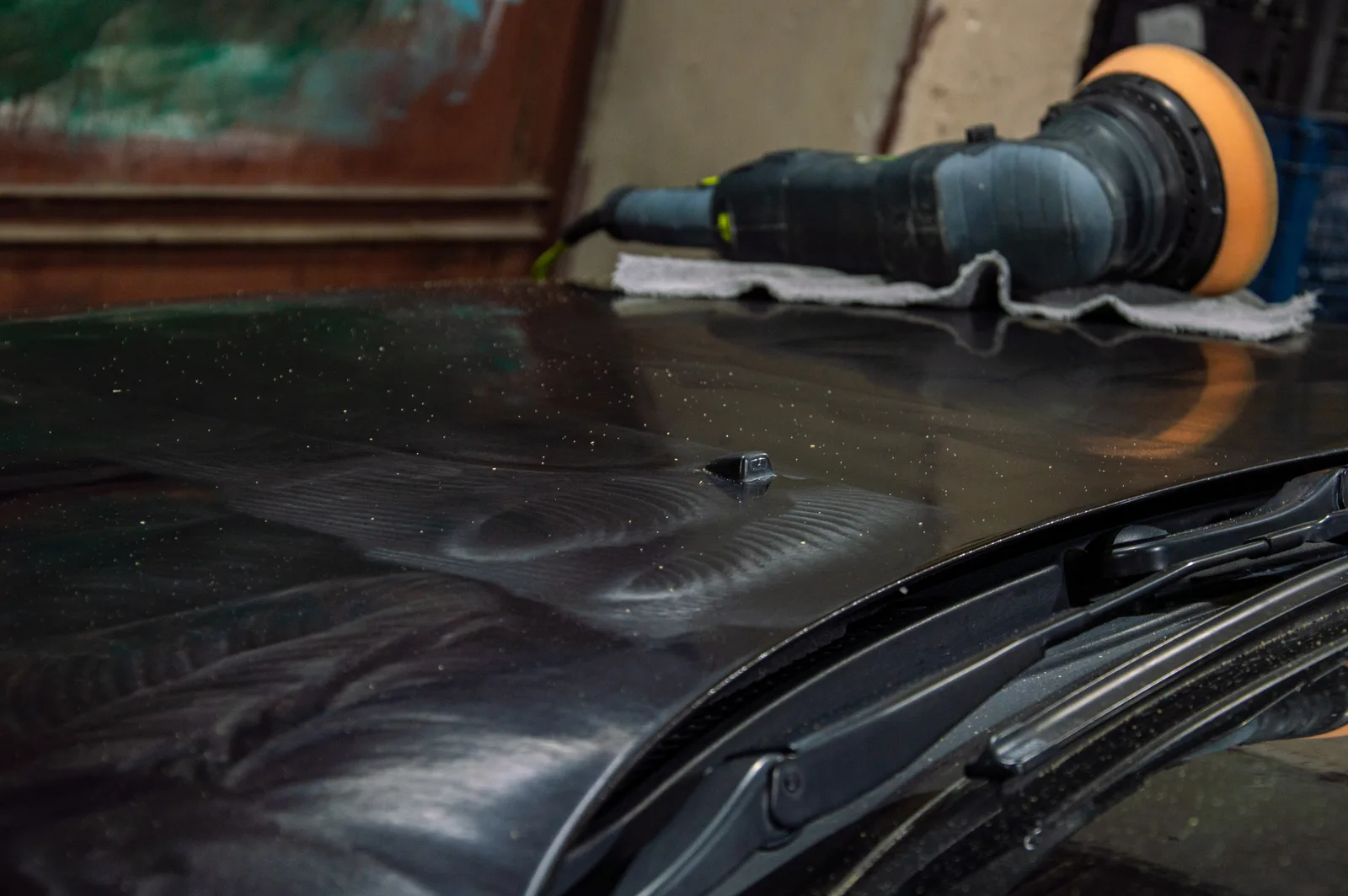 Detailer buffing swirl marks from a car's paint under bright lights in a detail bay