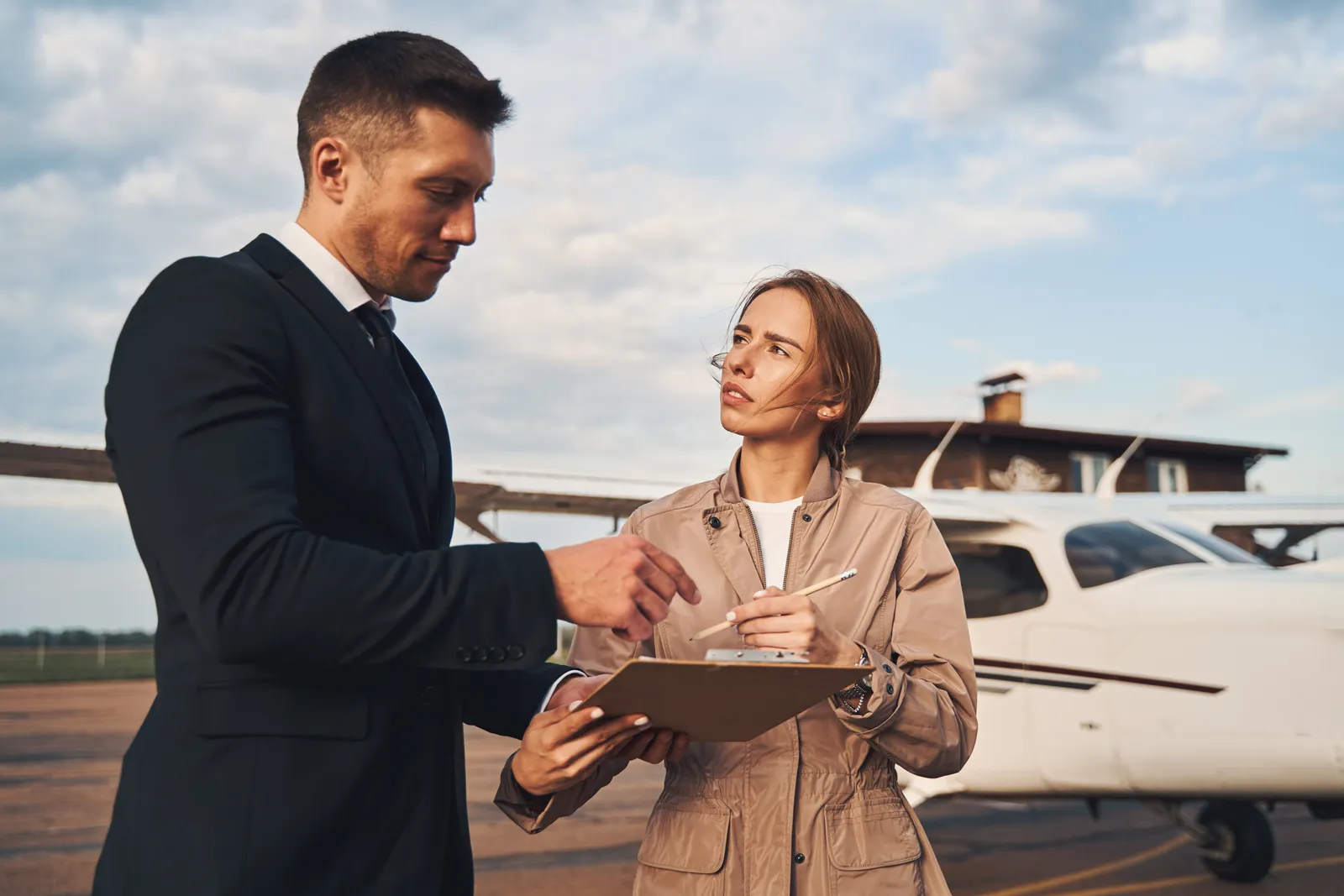 Aviation attorney reviewing an aircraft purchase agreement and FAA registration paperwork with a client beside a private airplane on the tarmac